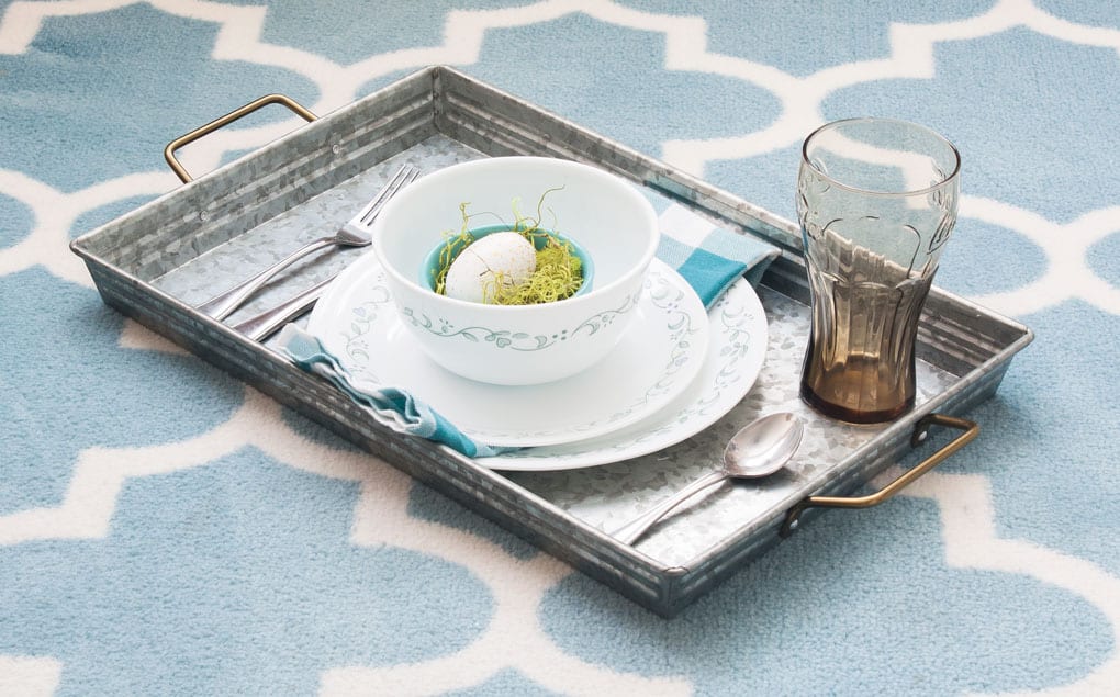 a metal tray holding a table setting napkin and decorative egg