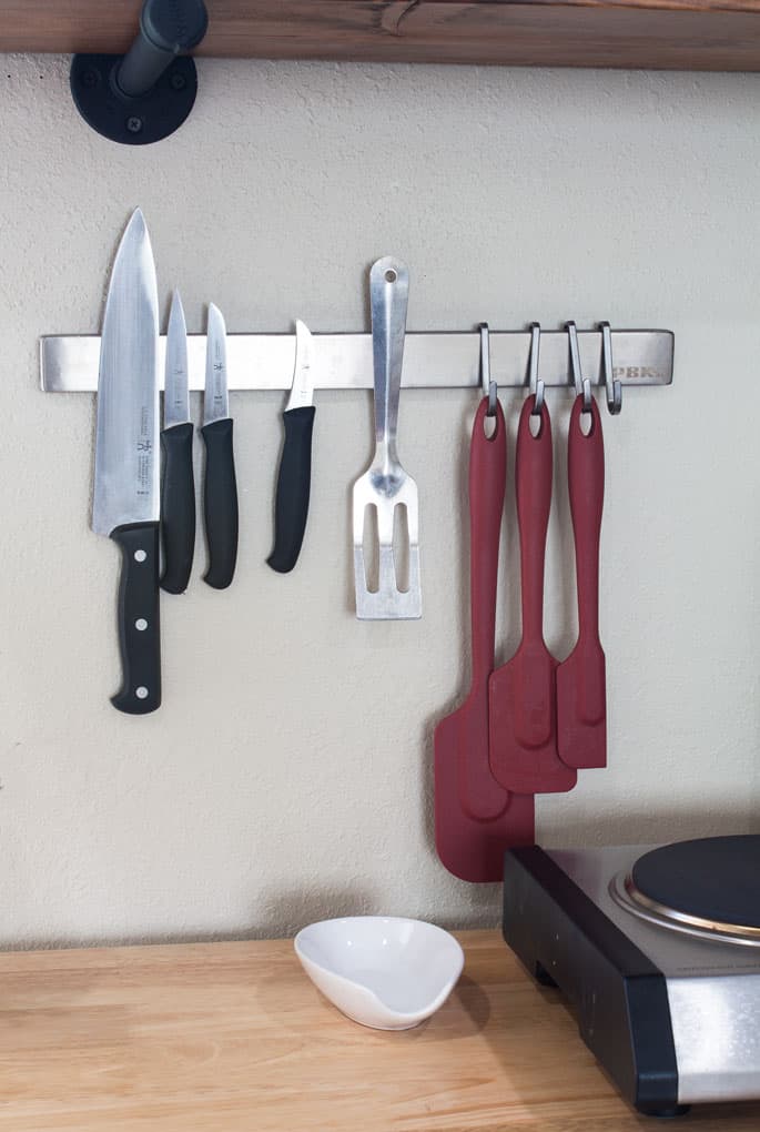 a closeup of magnetic knife strip mounted on a wall holding cooking utensils