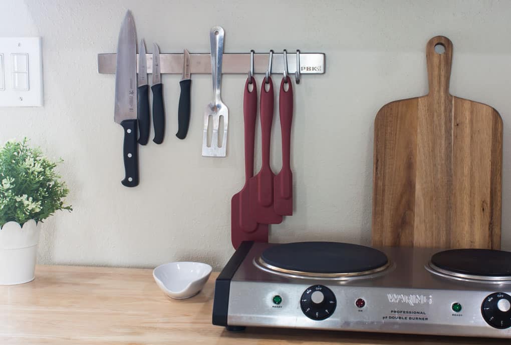 A kitchen island counter holding a double burner spoon rest cutting board and magnetic strip on the wall with utensils