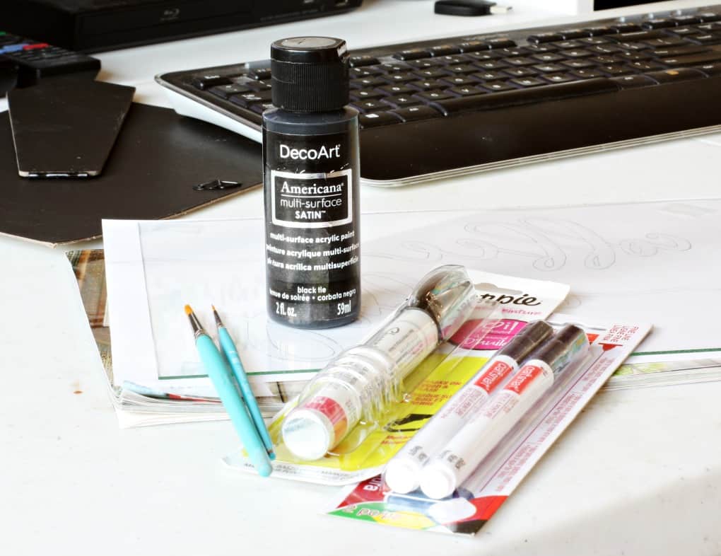 Paint brushes and paint pens sitting on table with papers and keyboard