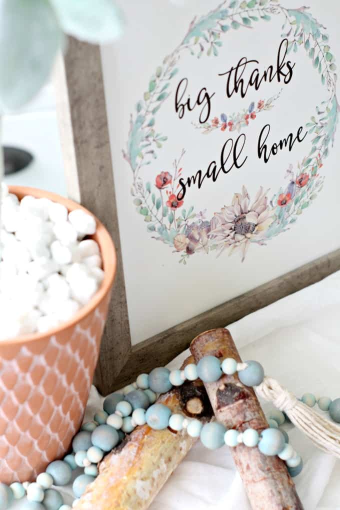 terra cotta pot and white rock with framed wall art that says big thanks small home birch branches and wooden bead garland on white table