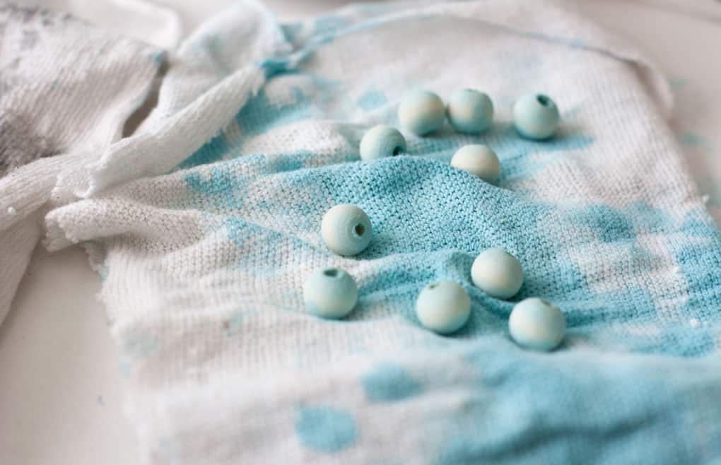 aqua painted wood beads on white cloth with paint covering the cloth