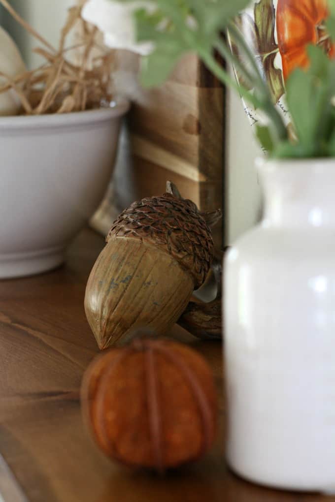 adding fall decor to a small kitchen wooden acorn on wood surface with white bowl and vase and cutting board in background