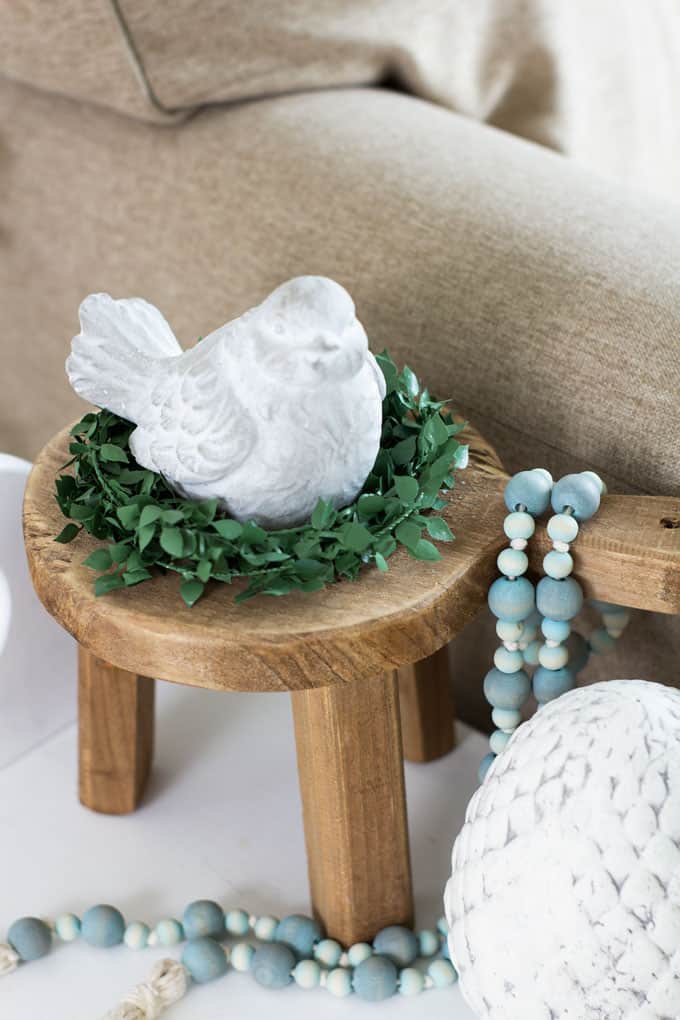 cement bird on mini stool with greenery and beads on table