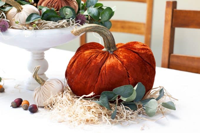 large orange velvet pumpkin with real stem on table with straw and acorns