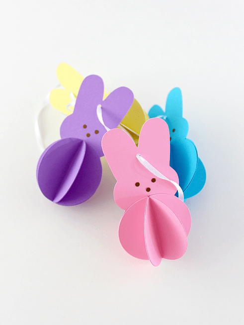 four multicolored paper peep bunnies with strings on white surface