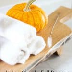 pedestal cutting board with soap dispenser cloths and pumpkin on top on white surface