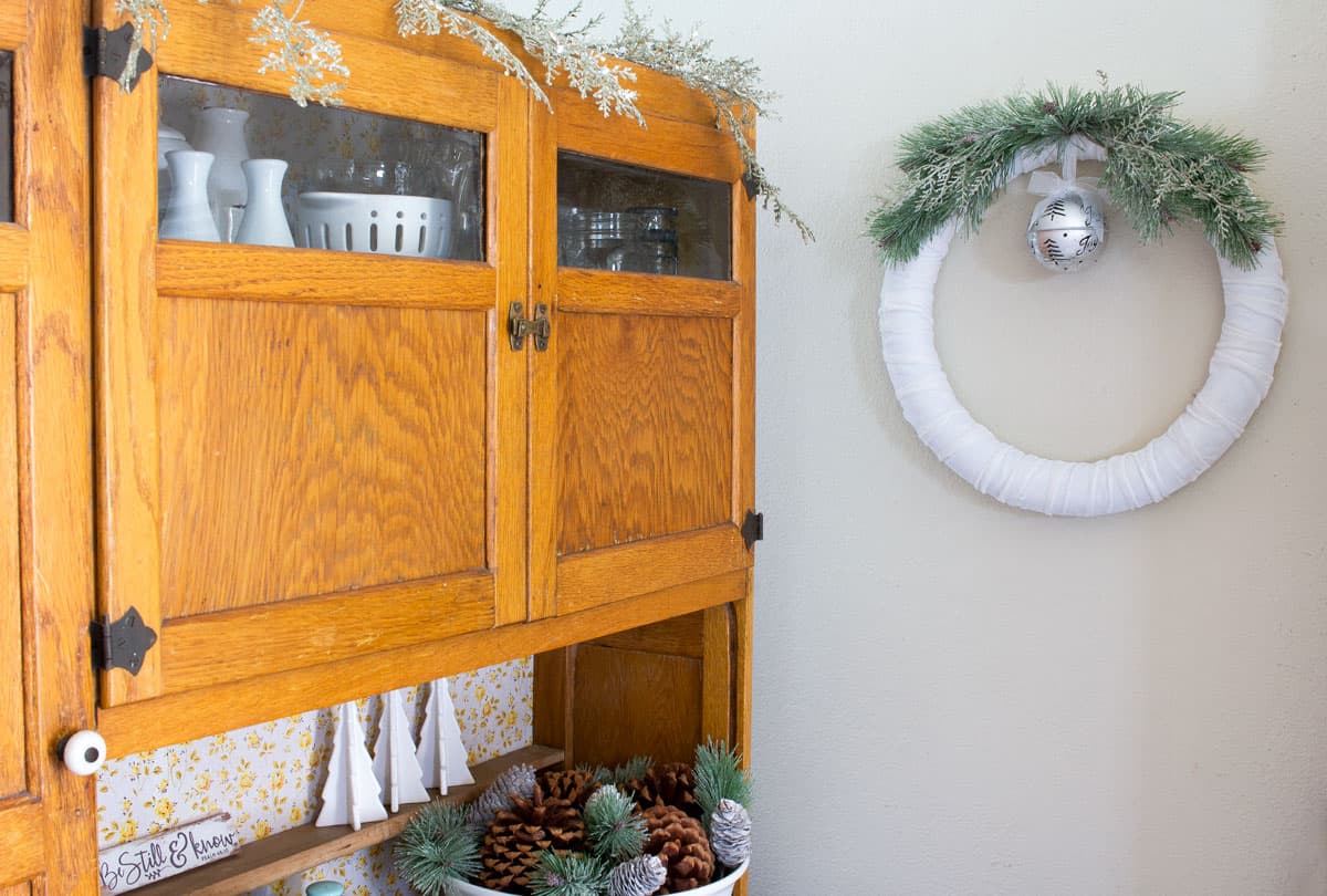 frosty velvet christmas wreath next to a bakers cabinet