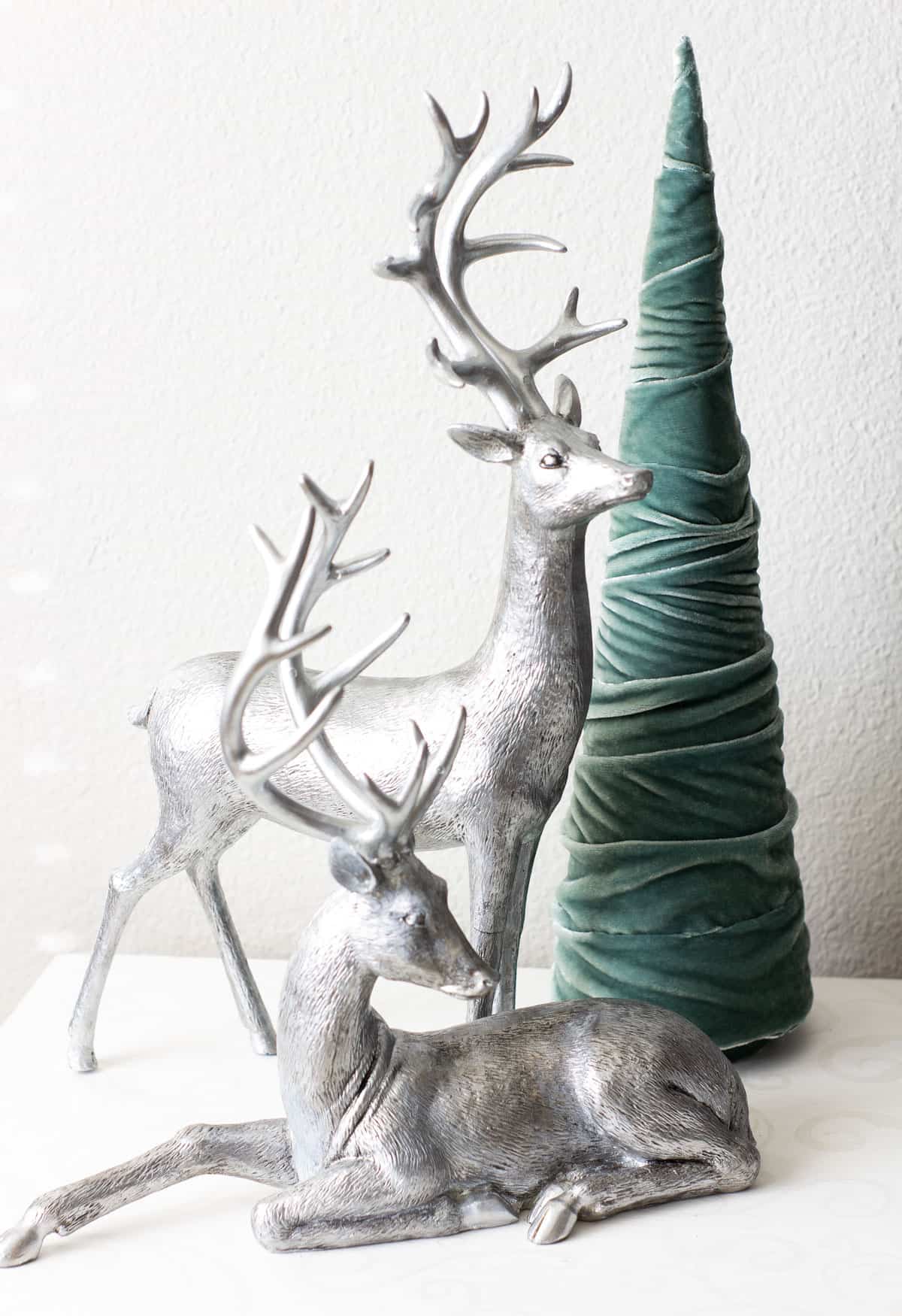 silver deer with a green velvet tree on a white surface