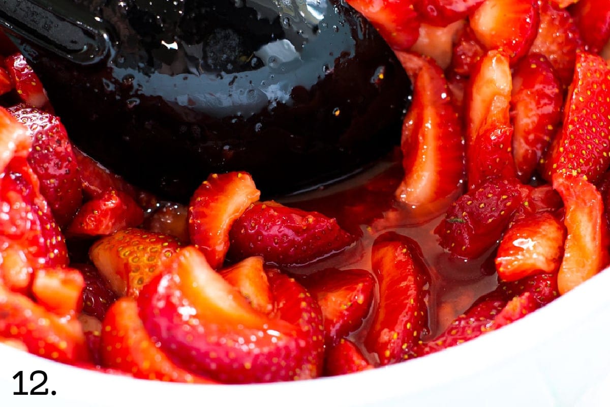 strawberry slices and juice in a bowl with black serving spoon