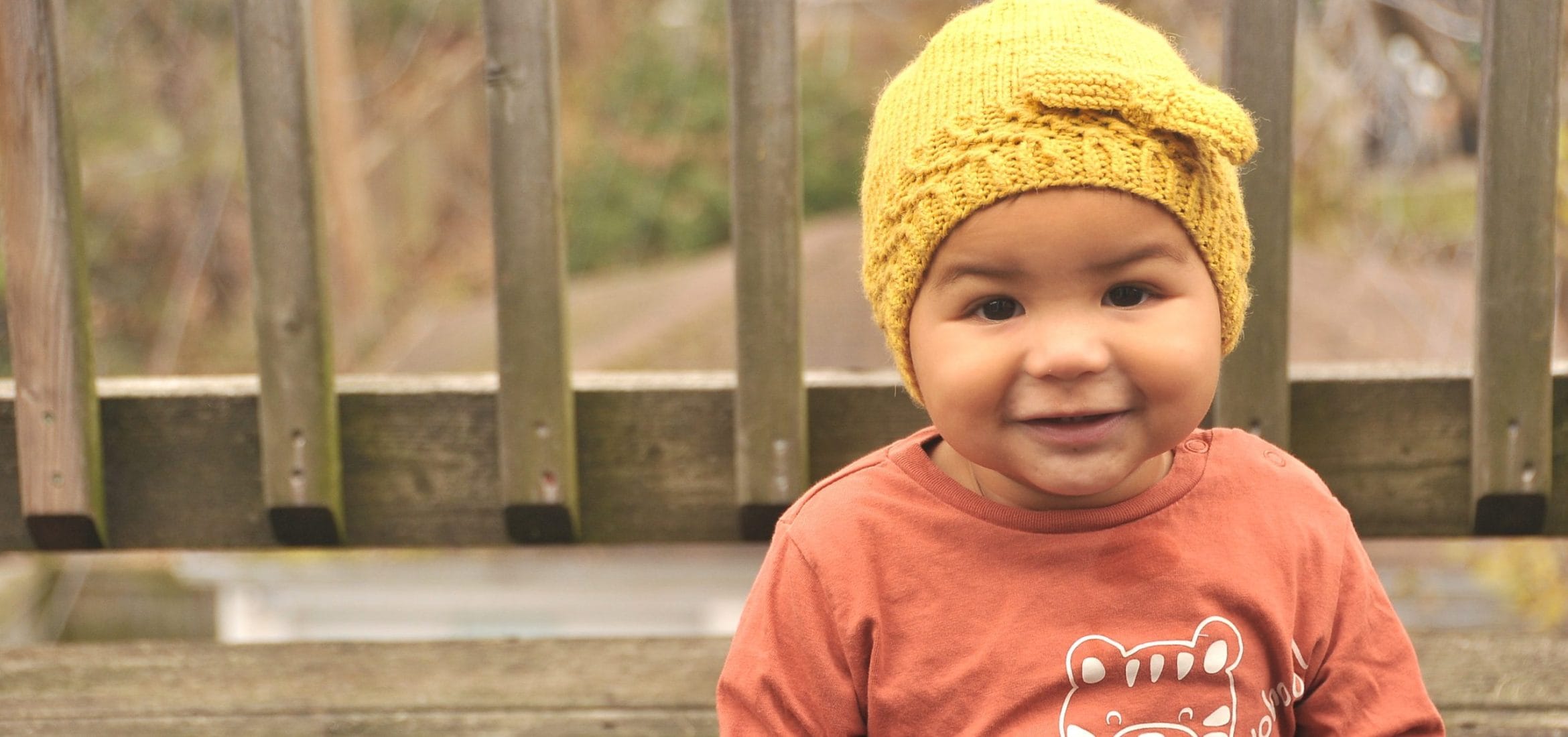 toddler in orange shirt with yellow crocheted beanie