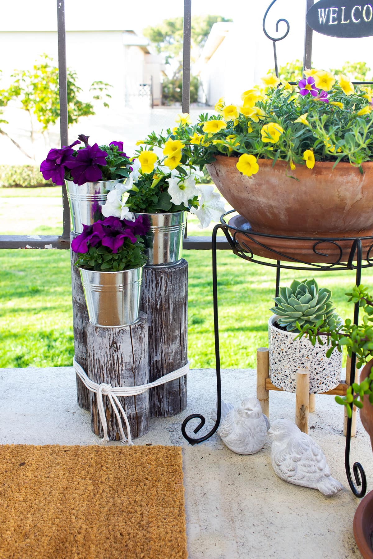 metal buckets with petunias on wood pilings with other patio plants and decor