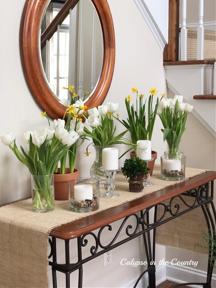 tulips and daffodils in vases on entryway table with mirror on wall