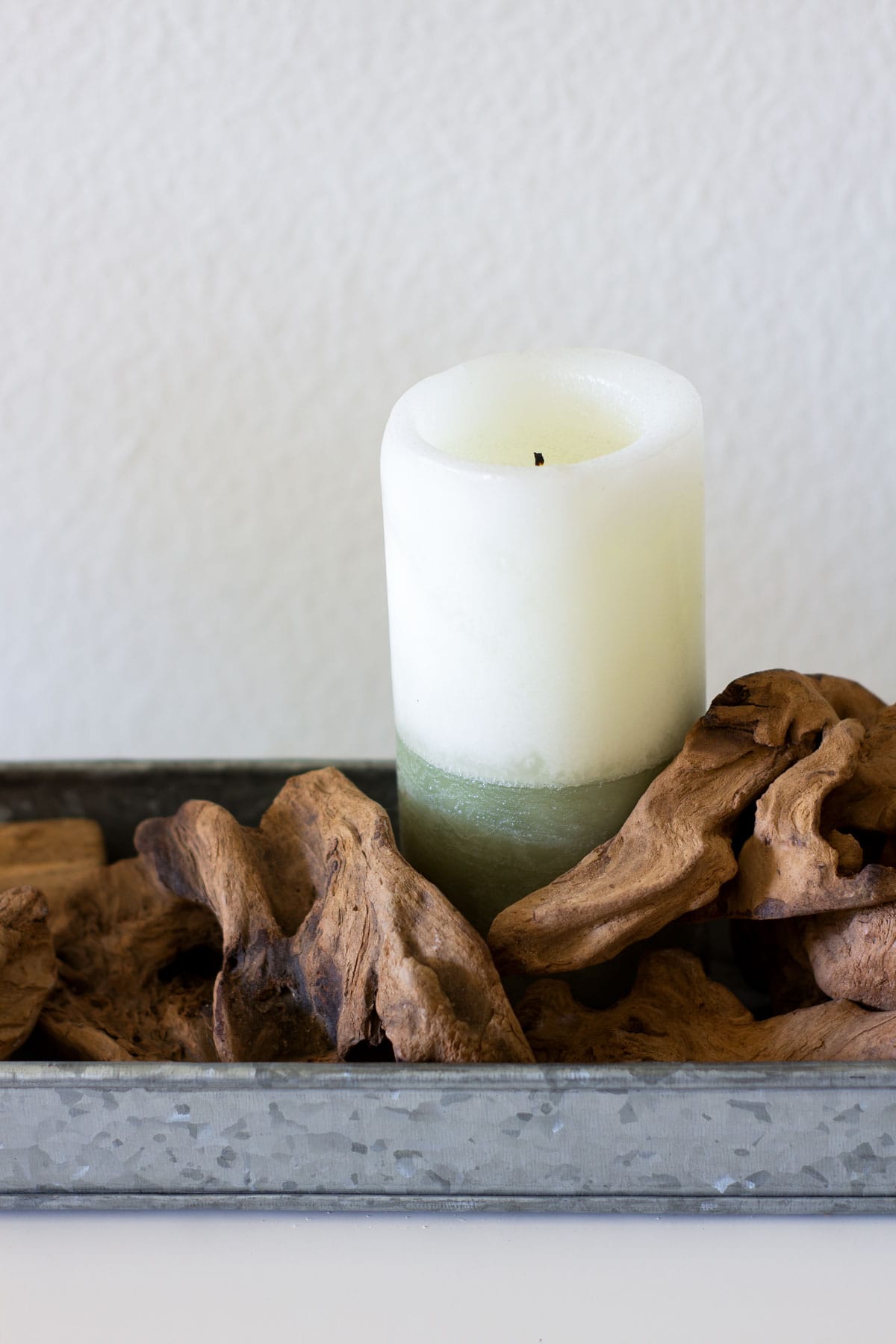 sage and white candle in tray with driftwood