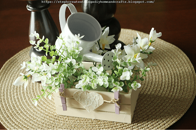 crate with flowers and watering can on woven mat