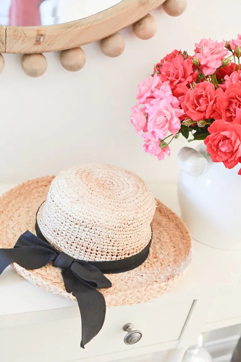 straw hat and vase with pink and red flowers on shelf
