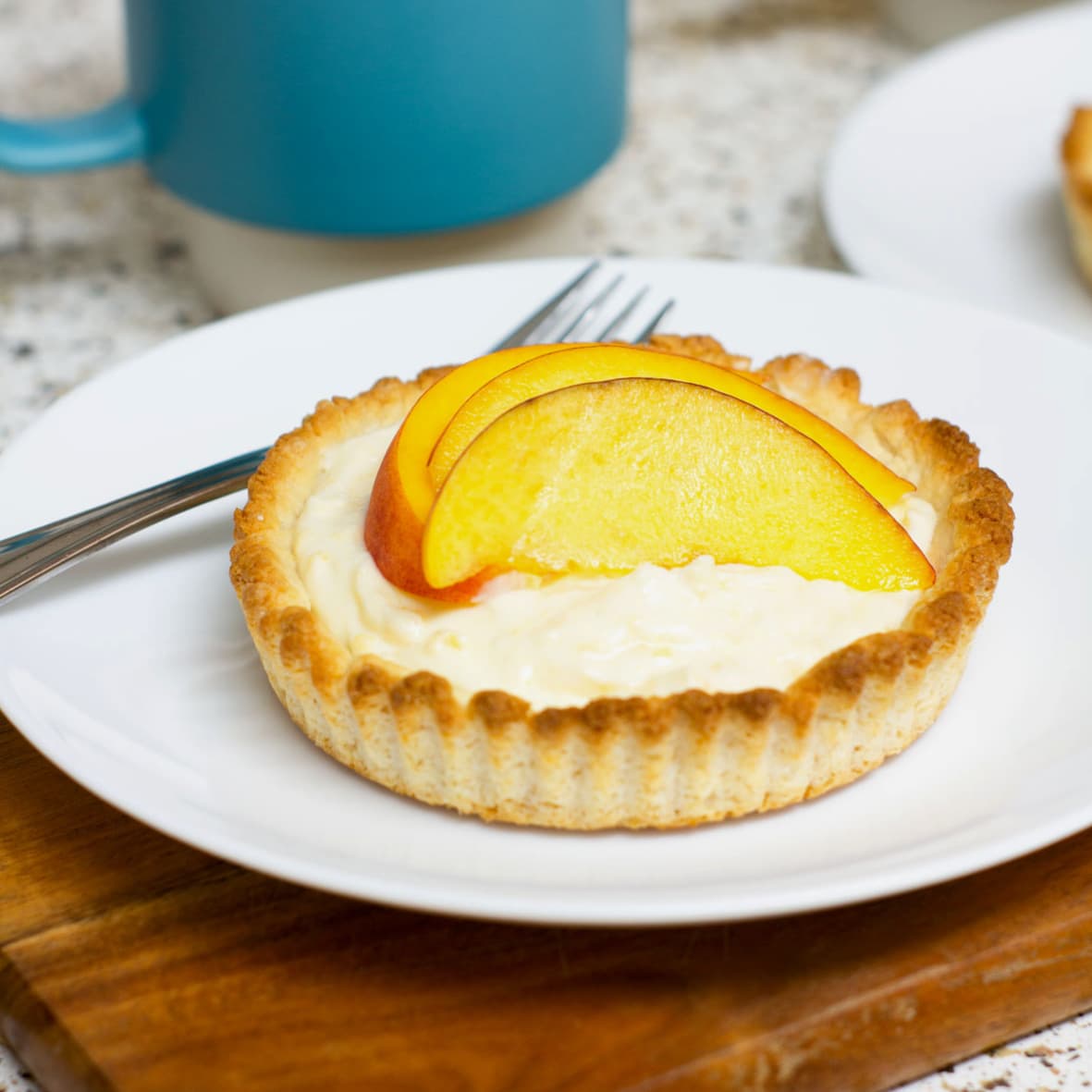 easy and creamy fresh peach tartlet on white plate with fork on cutting board