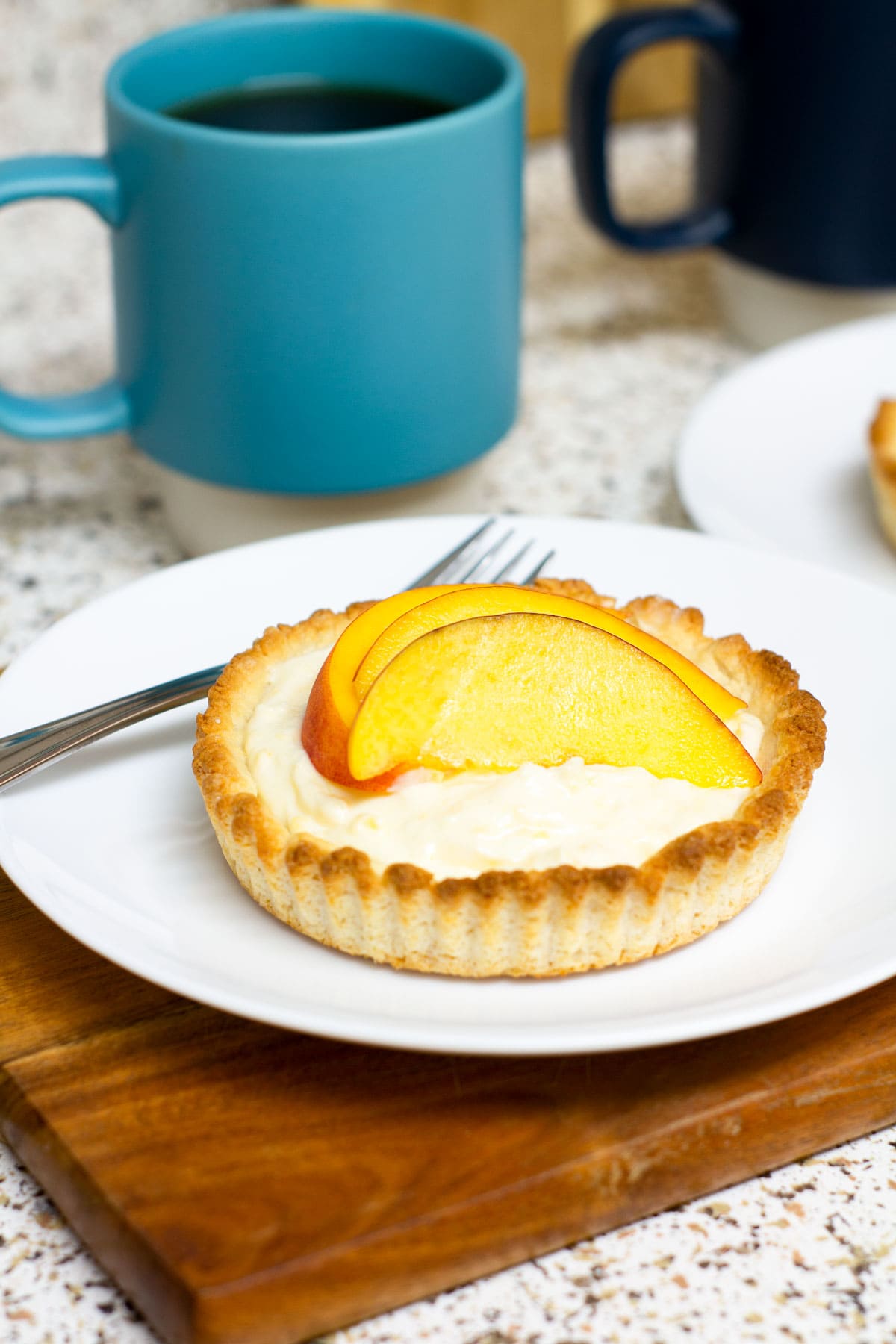 easy creamy fresh peach tartlet on white plate with coffee in background
