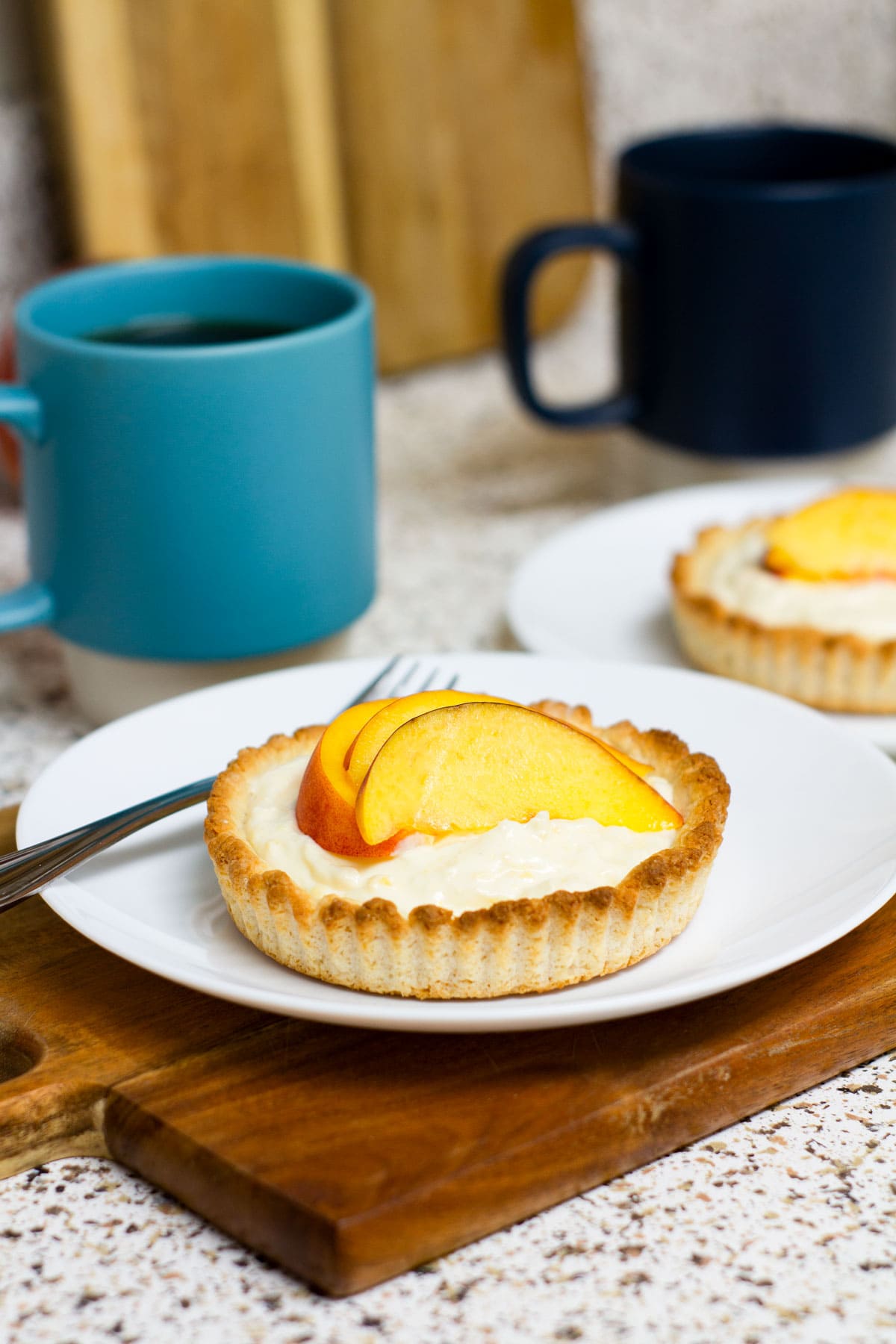 easy creamy fresh peach tartlet on white dish with fork on cutting board with coffee cup
