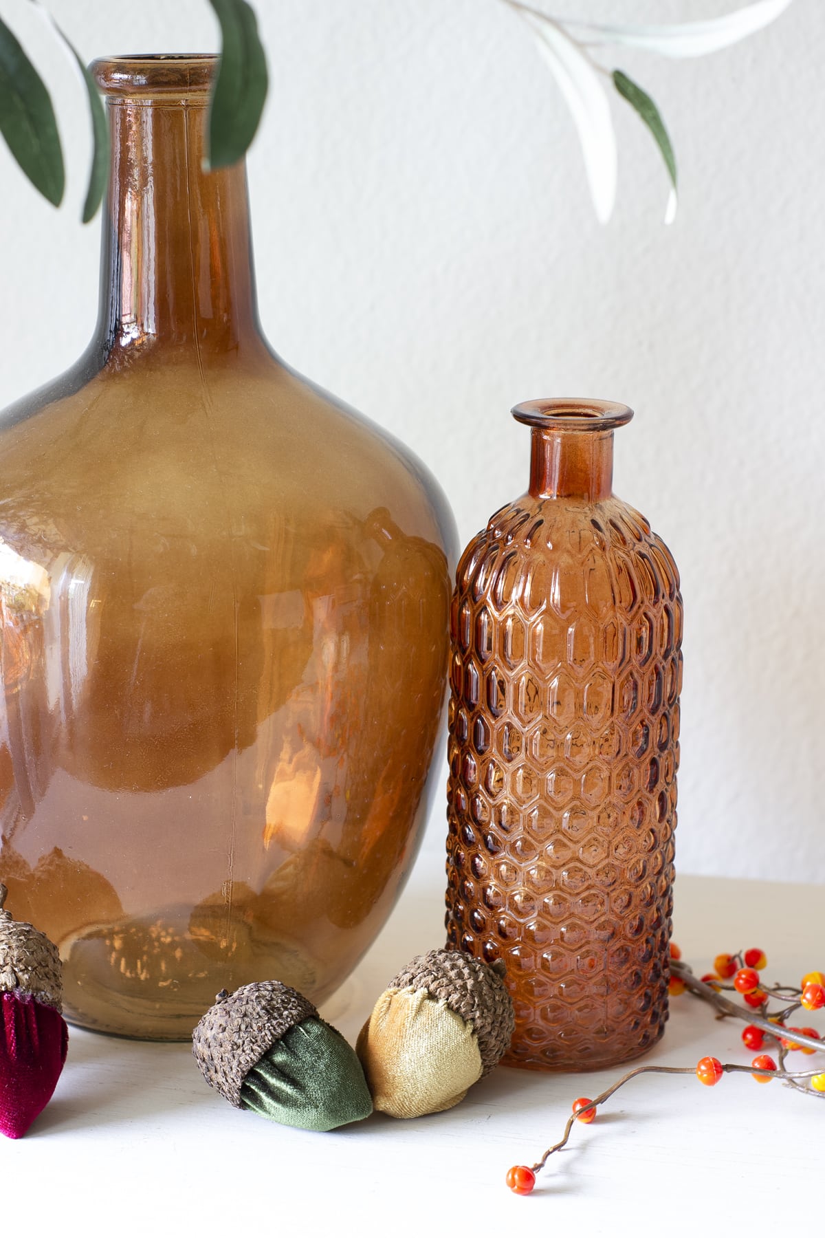 amber bottles on shelf with velvet acorns in different colors and garland of berries