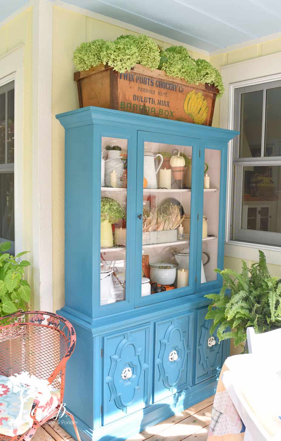 blue chine cabinet on outside porch with white dishes and plants