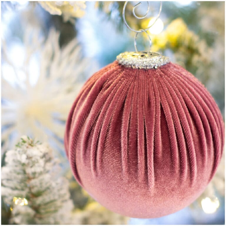 burgundy velvet christmas ornament hanging in tree with lights and blurred ornament in foreground