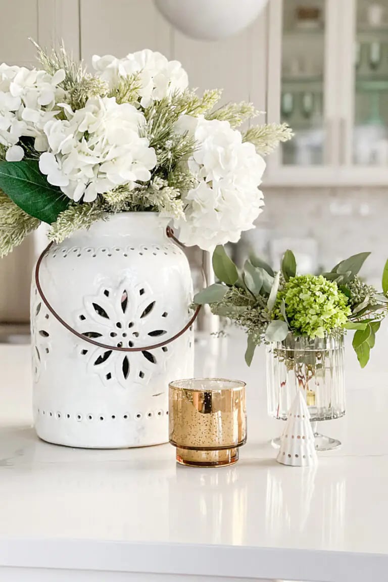 florals and greenery in winter lanterns and candle in cup on white surface