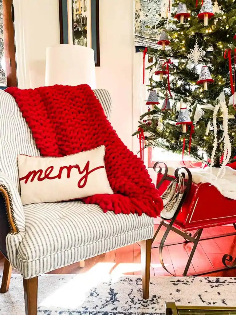 red knit blankets on chair with merry pillow and christmas tree in background