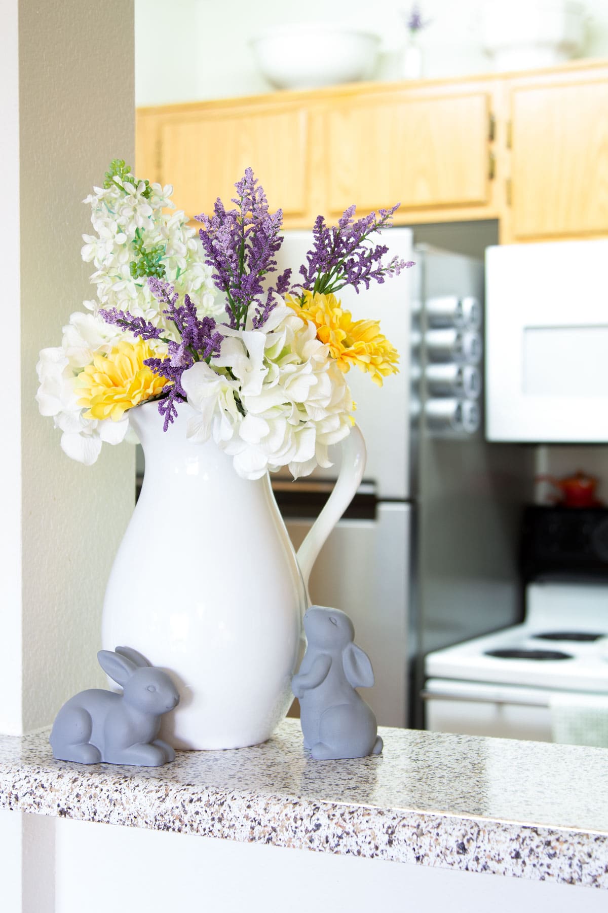 white pitcher with spring flowers and gray bunnies in kitchen