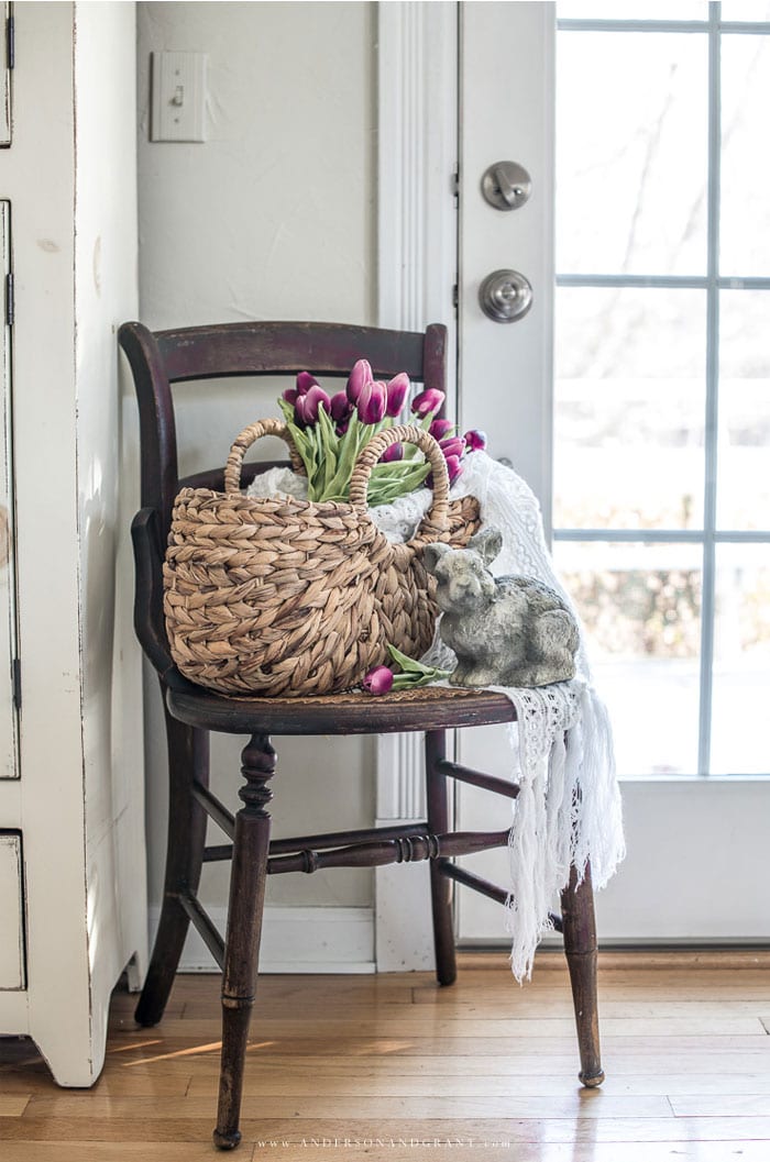 wooden chair next to glass paned door with basket holding tulips a bunny and throw blanket