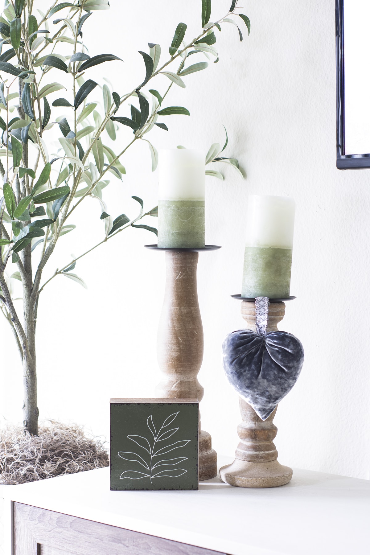 wooden candlesticks with green and white candles and velvet heart with leaf sign on console