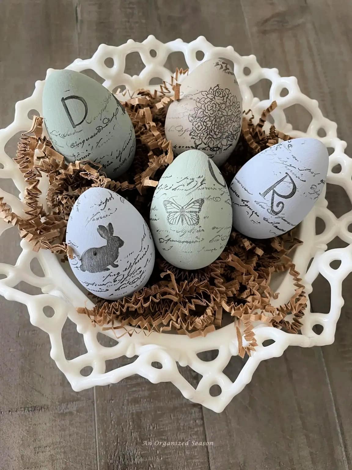 painted and stamped easter eggs in glass dish with brown paper grass