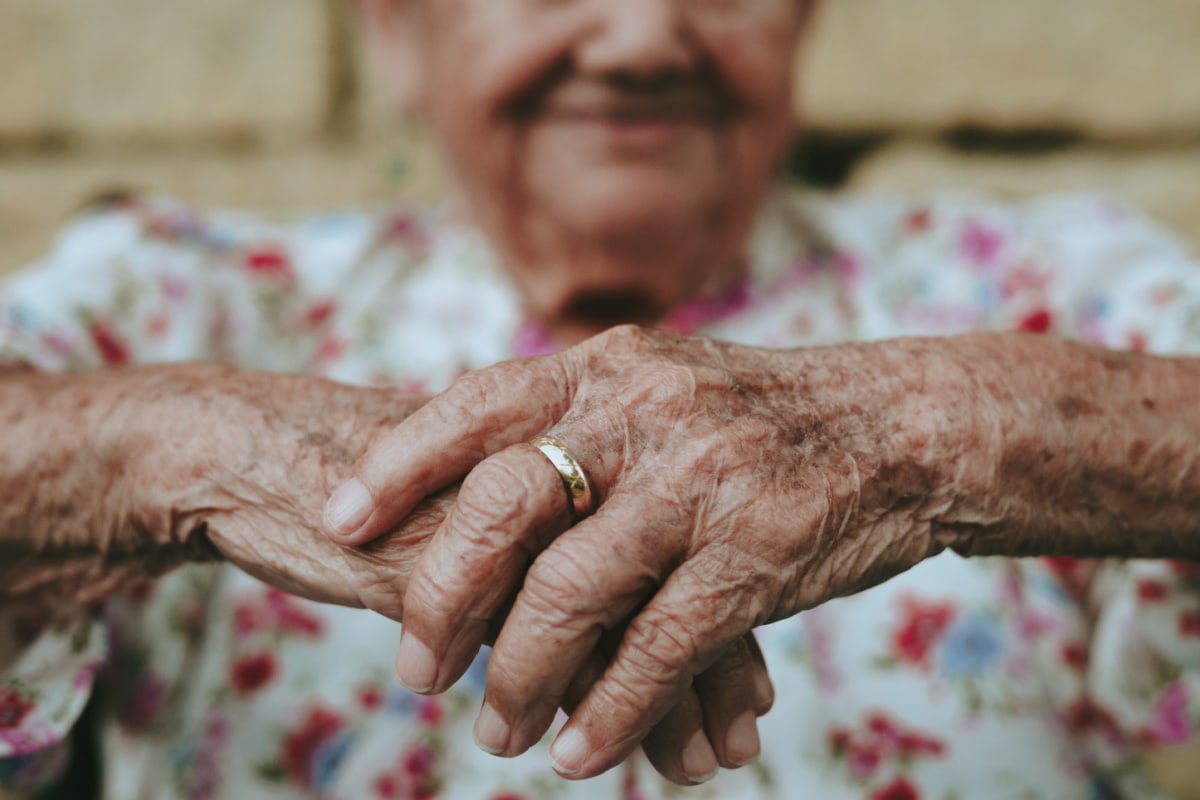 old woman hands with ring and face of woman in background