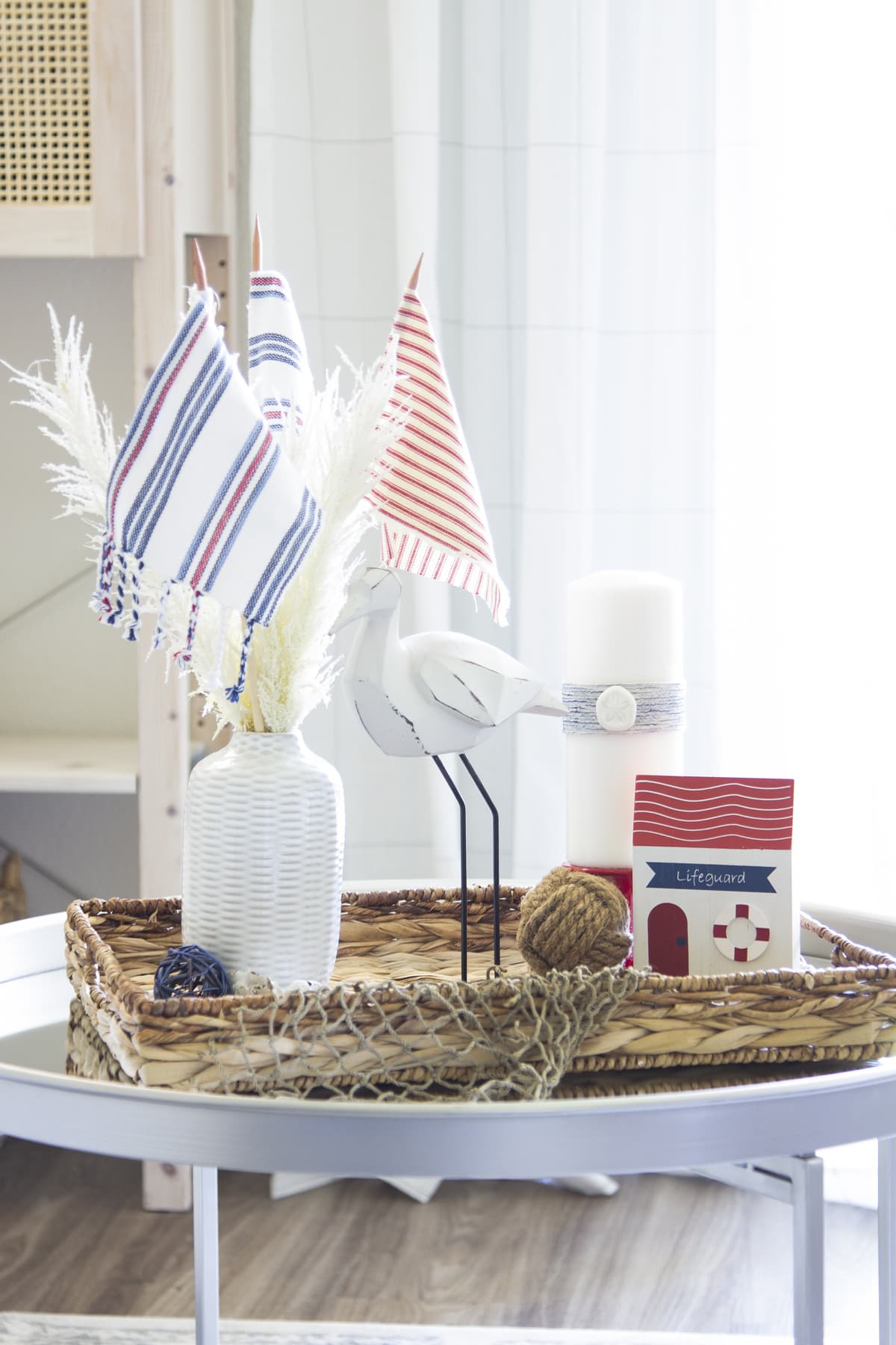adding red white blue to a summer vignette with vase and beach grass bird figurine and candle on white holder with seagrass tray