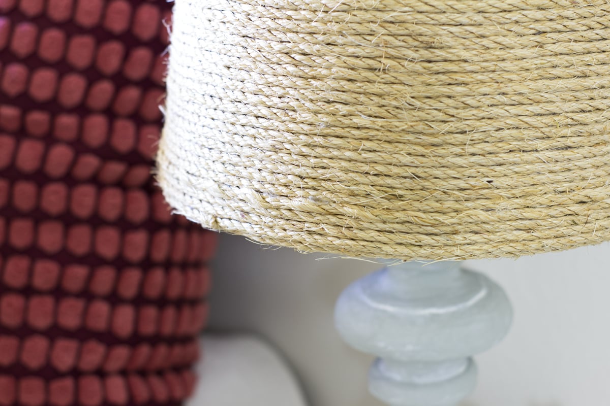 woven lampshade with cement base next to burgundy pillow