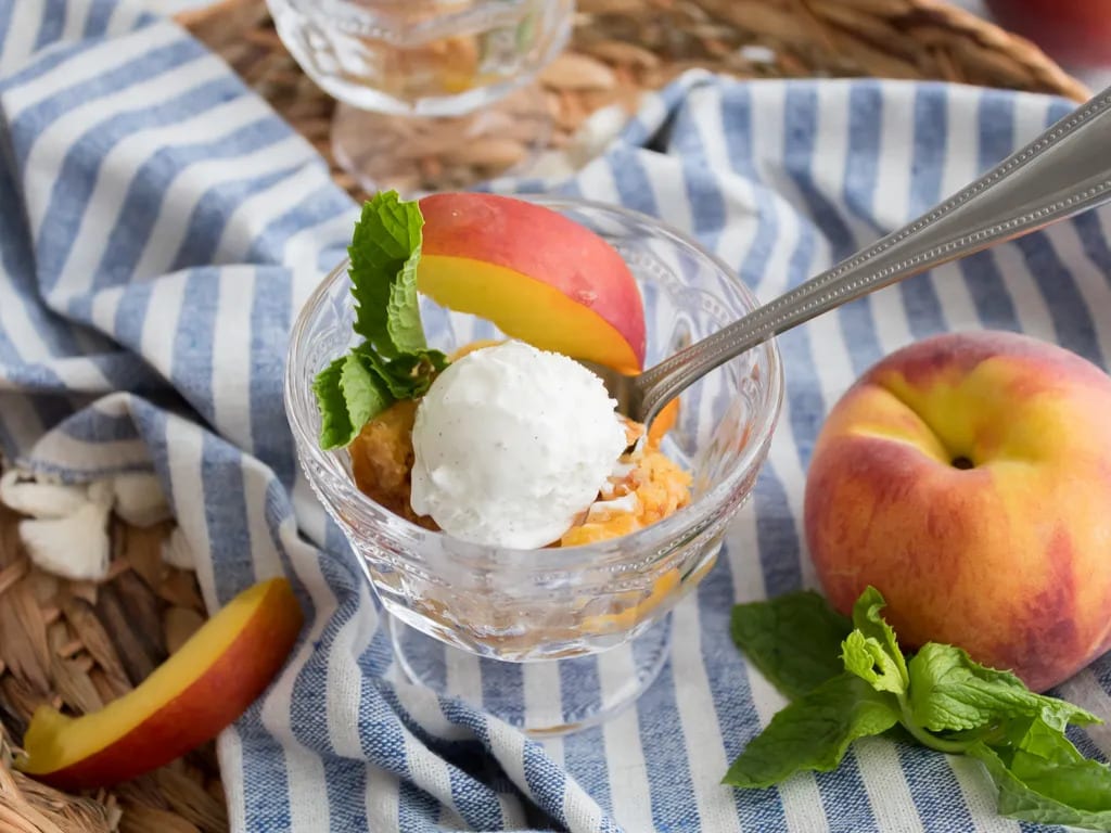 peach dessert in galss with peaches on table on top of blue and white stripe linen