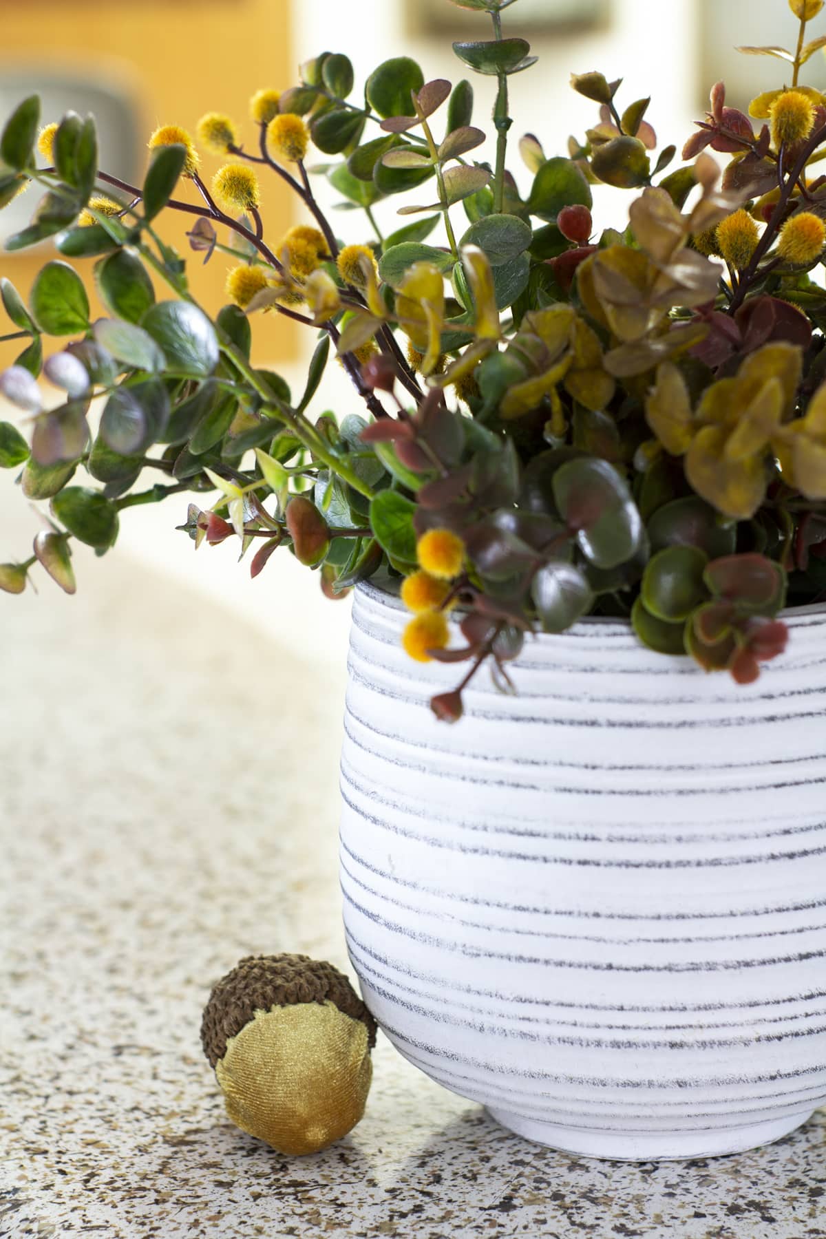 fall floral arrangement in white pot and velvet acorns on kitchen counter