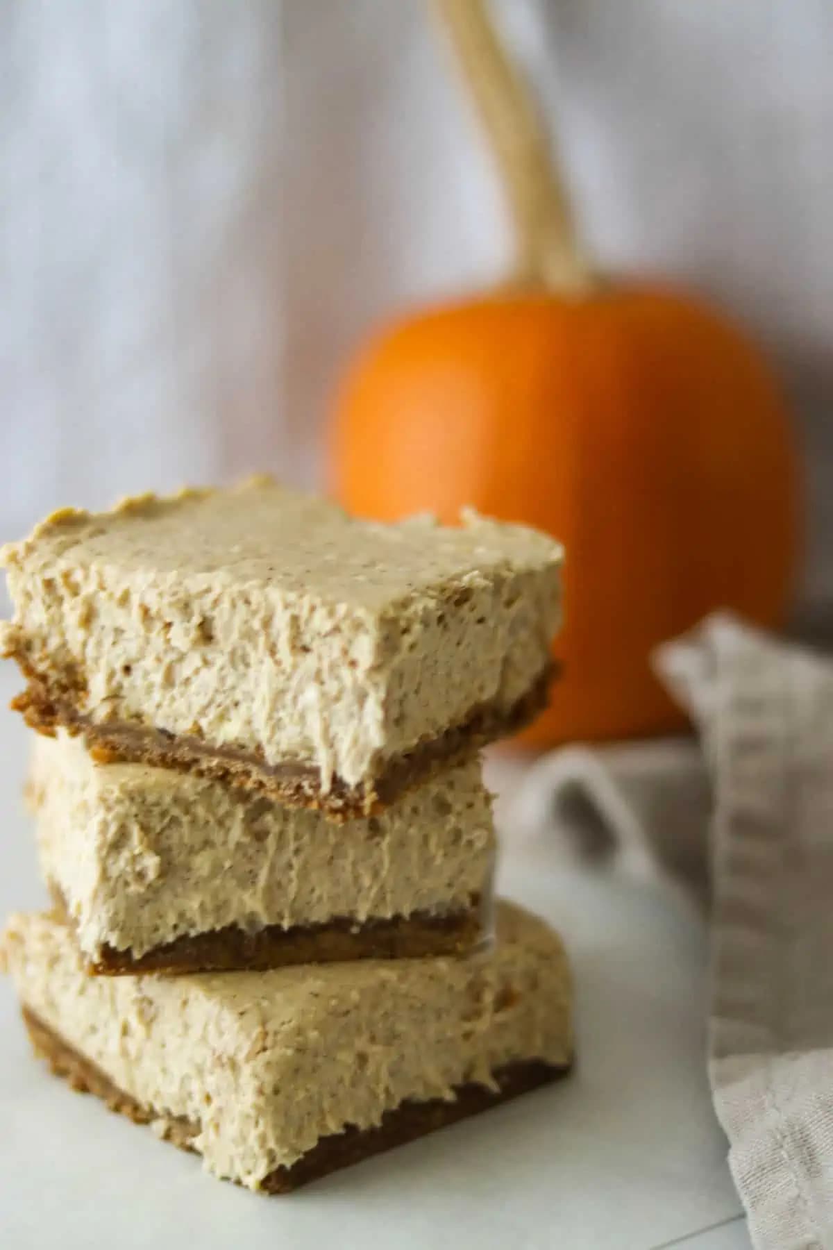 stack of pumpkin cheesecake bars with pumpkin in background