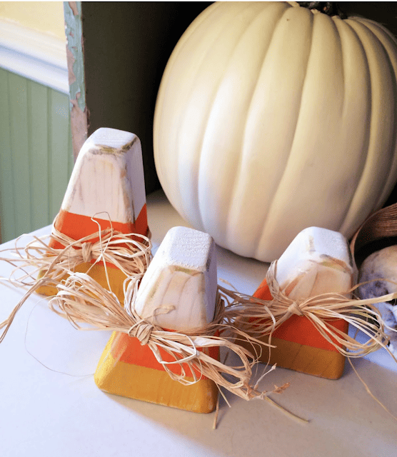 wood candy corns with raffia ribbon and pumpkin in background