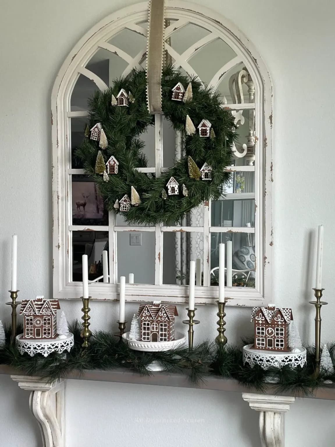 gingerbread houses on sideboard with candles and gingerbread wreath on mirrored wall