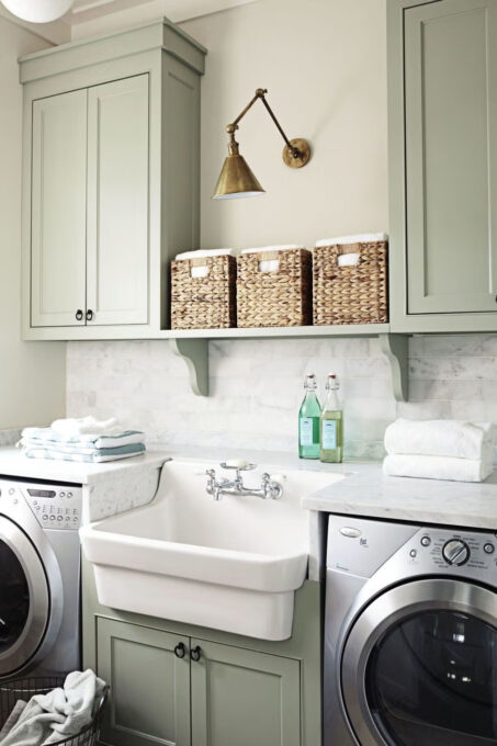 sage green cabinet paint colors laundry room with washer and dryer and woven baskets with gold accents